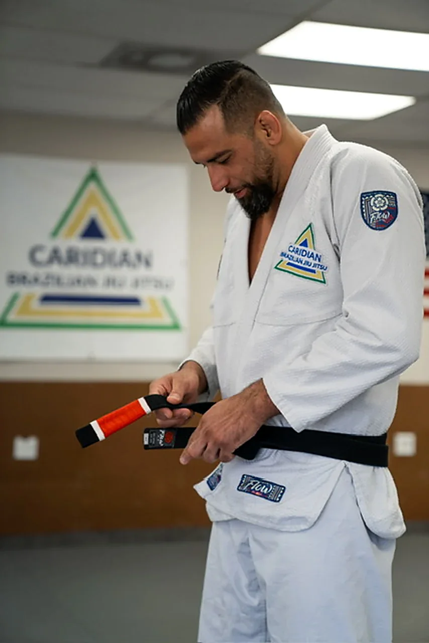 Alan Ribeiro adjusting his black belt in a white gi at Caridian