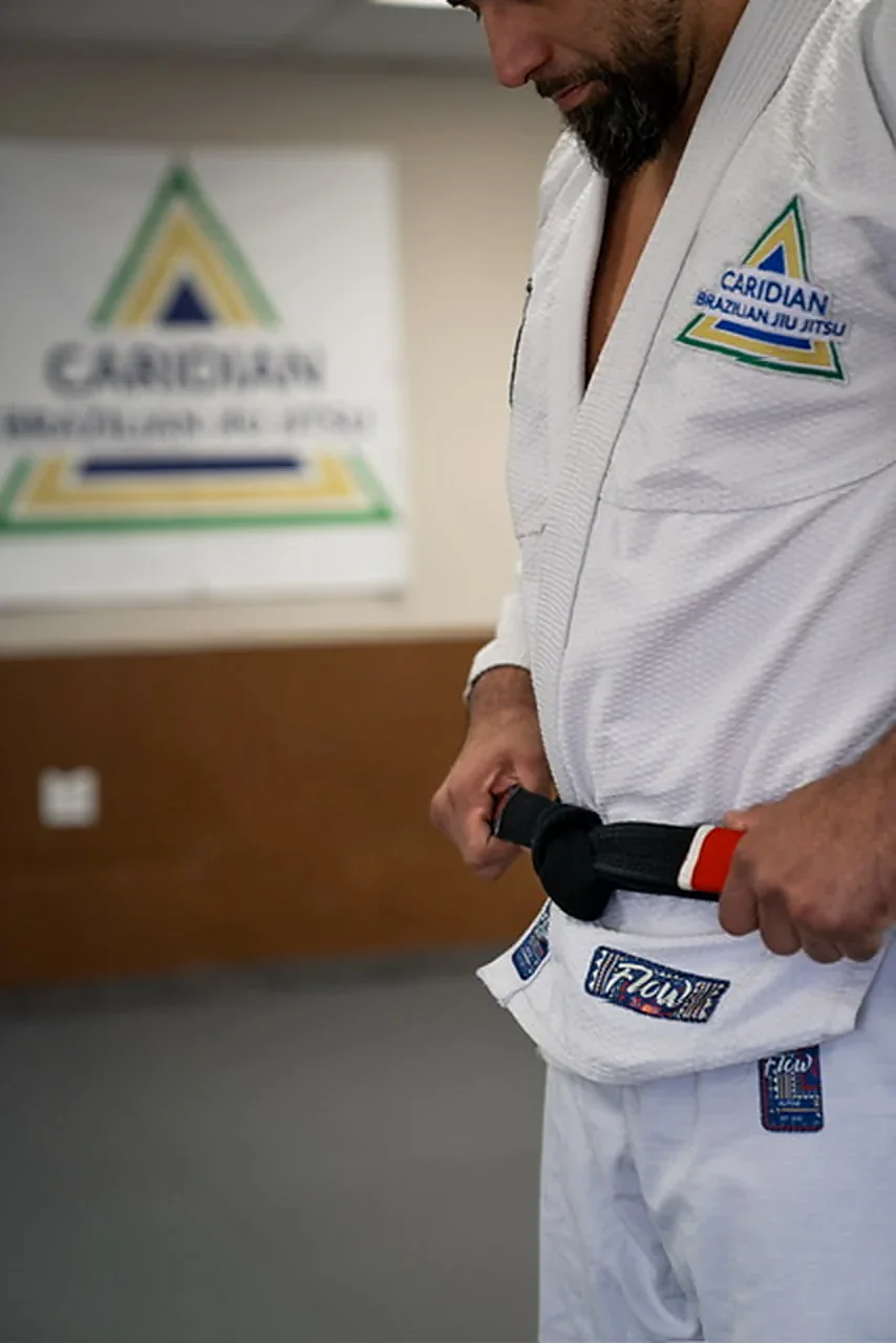 Alan Ribeiro adjusting his belt beside the Caridian Brazilian Jiu-Jitsu sign