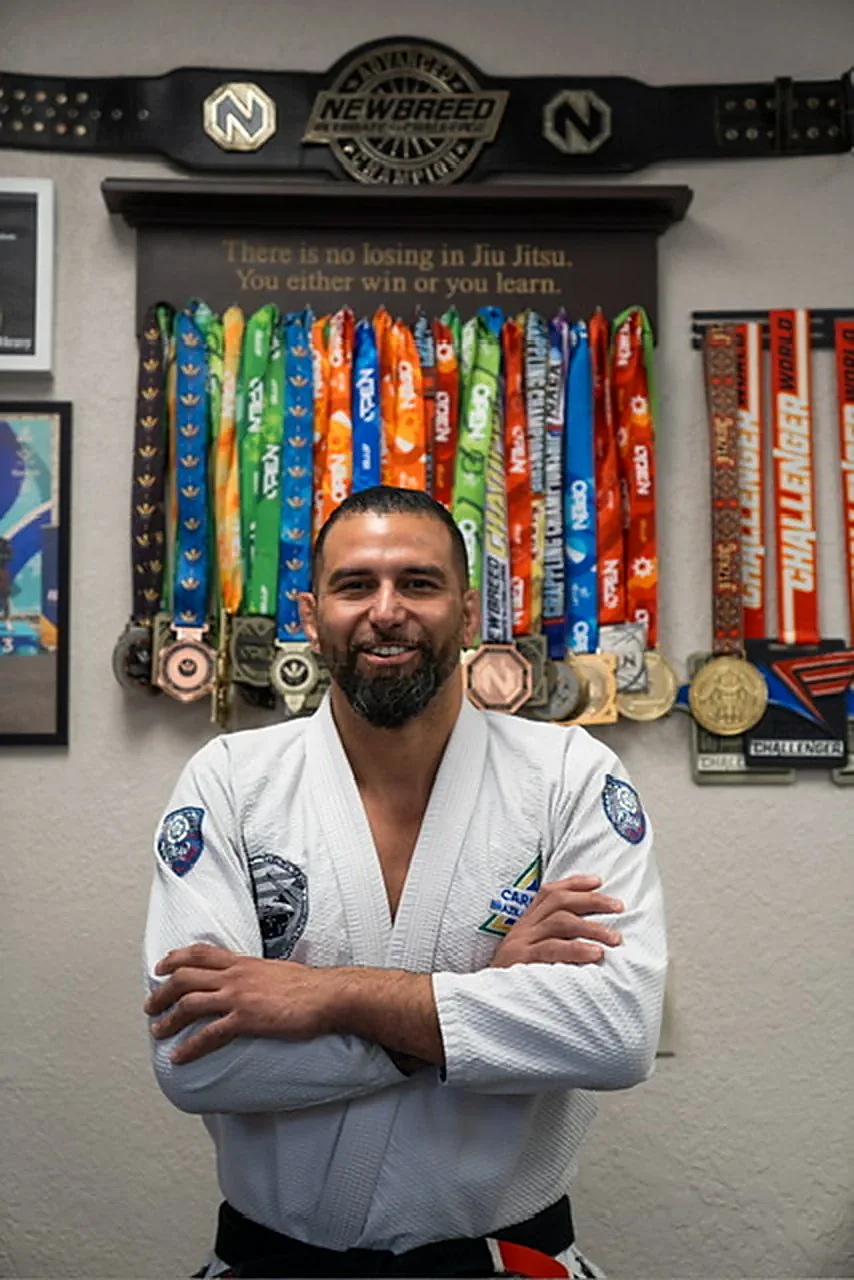 Alan Ribeiro in his gi in front of a wall of medals and the Caridian sign